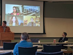 people watch scholars on a projector screen as one of the virtual presenters speaks. 
